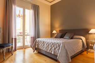 Ein Schlafzimmer mit einem Bett, zwei Nachttischlampen, einem Sessel und Blick durch eine Glastür.