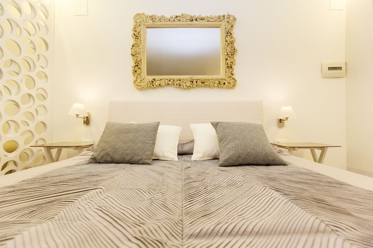 Habitación de hotel con una cama grande, dos mesitas de noche, un espejo en la pared y un panel decorativo.