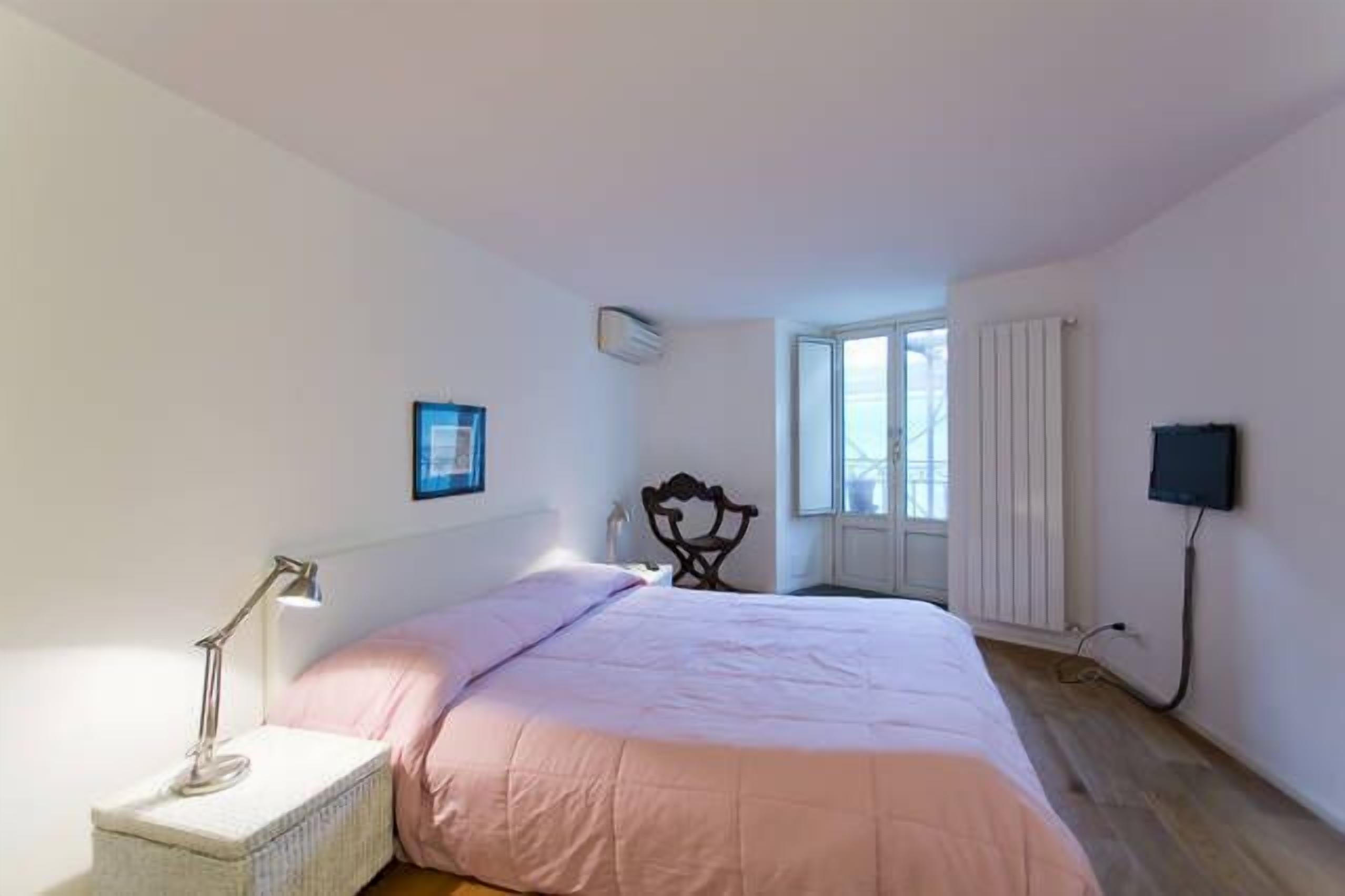 Un dormitorio con cama, lámpara de noche y ventana.
