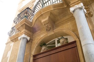 Fachada de edificio con arquitectura clásica, con columnas, un balcón con barandilla de hierro forjado y una puerta de madera grande.