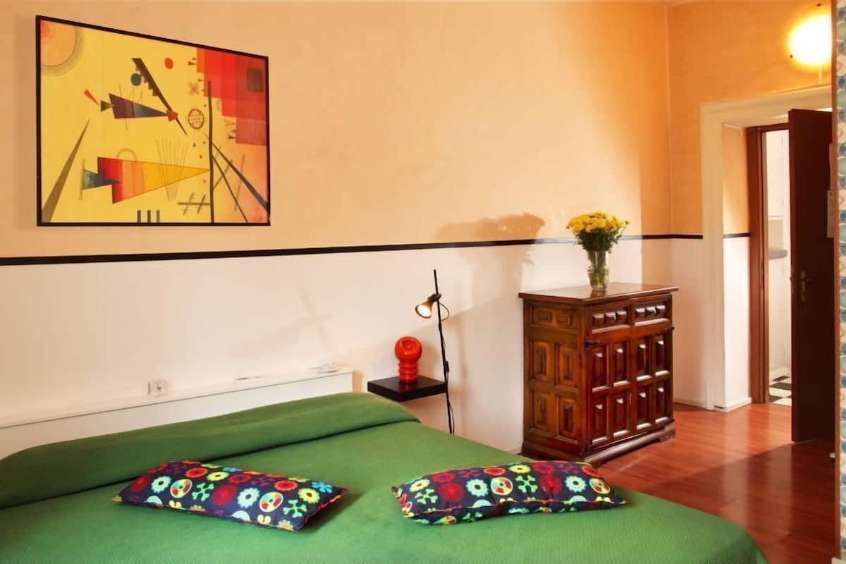 A room with a bed, a wooden cabinet, a wall-mounted painting, and a door leading to another room.