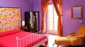 A bedroom with a bed, a chair, a refrigerator, and a window with curtains. - Prince of Via Veneto DELUXE (Rome)
