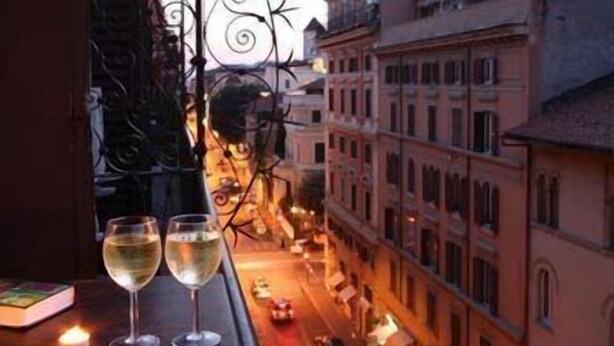 A view from a window overlooking a street with buildings, two glasses of white wine, and a candle on a table. - Prince of Via Veneto DELUXE (Rome)