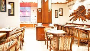 A restaurant with wooden furniture, a central counter, and framed artwork on the walls. - The Residency Mumbai (GUNDAVALI, ANDHERI)