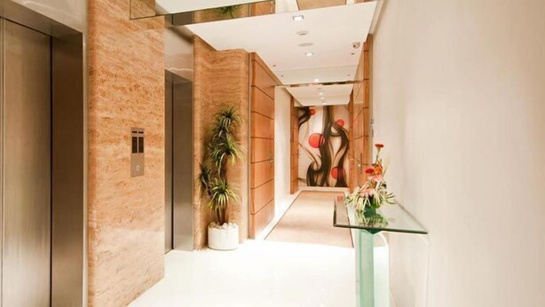 A modern hallway with a wooden panel wall, a potted plant, and a glass table with flowers. - The Residency Mumbai (GUNDAVALI, ANDHERI)