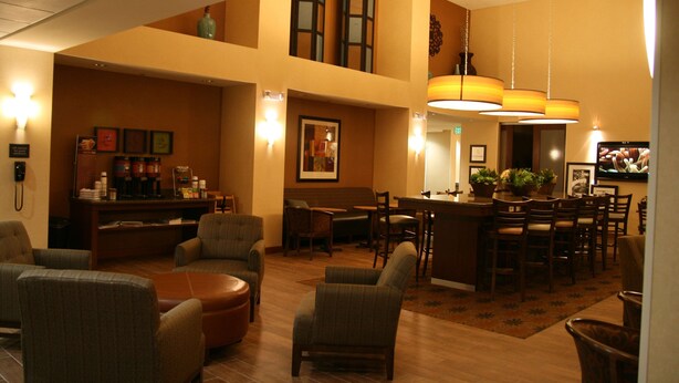 A spacious lobby with a high ceiling, a bar area, and multiple seating arrangements including chairs and a round table. - Hampton Inn & Suites Pueblo/North (Pueblo)