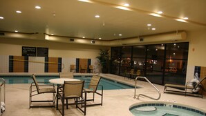 An indoor pool area with a table and chairs, a lifeguard sign, and a view of the city through large windows. - Hampton Inn & Suites Pueblo/North (Pueblo)