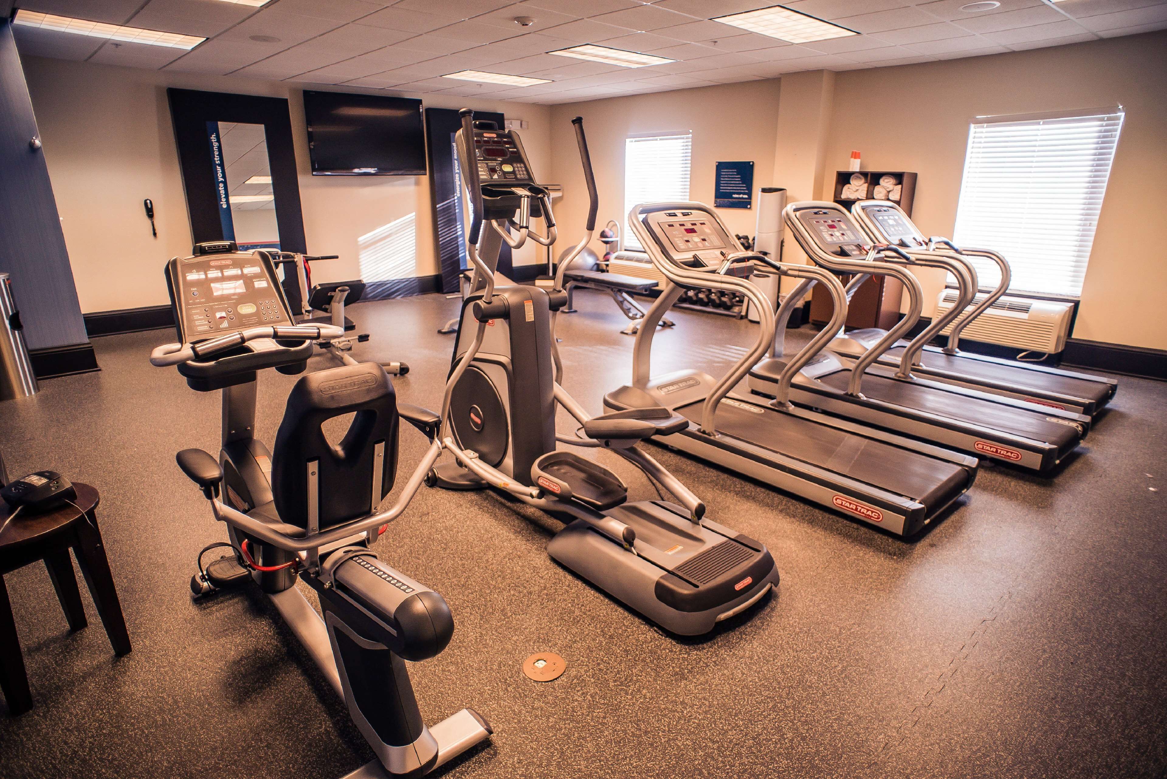 A fitness center with various cardio machines, a television, and a mirror on the wall.