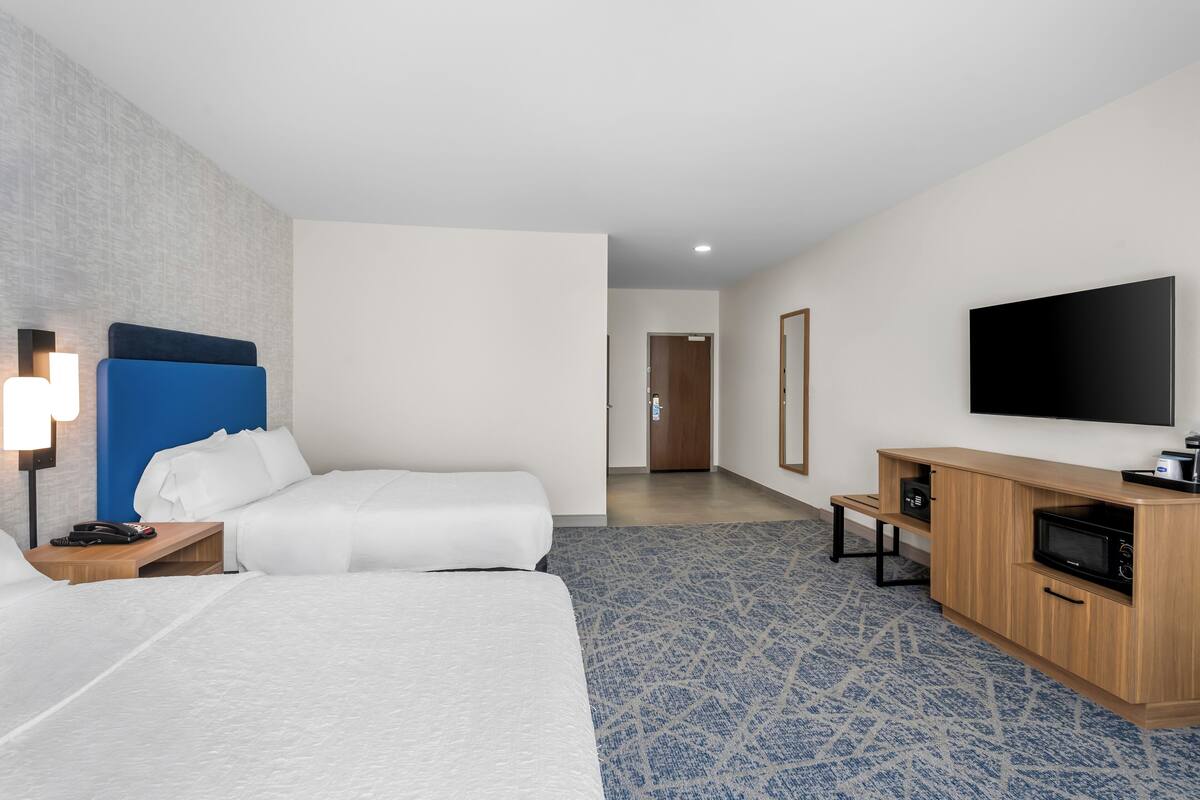 A hotel room with two beds, a TV, a desk, and a microwave.