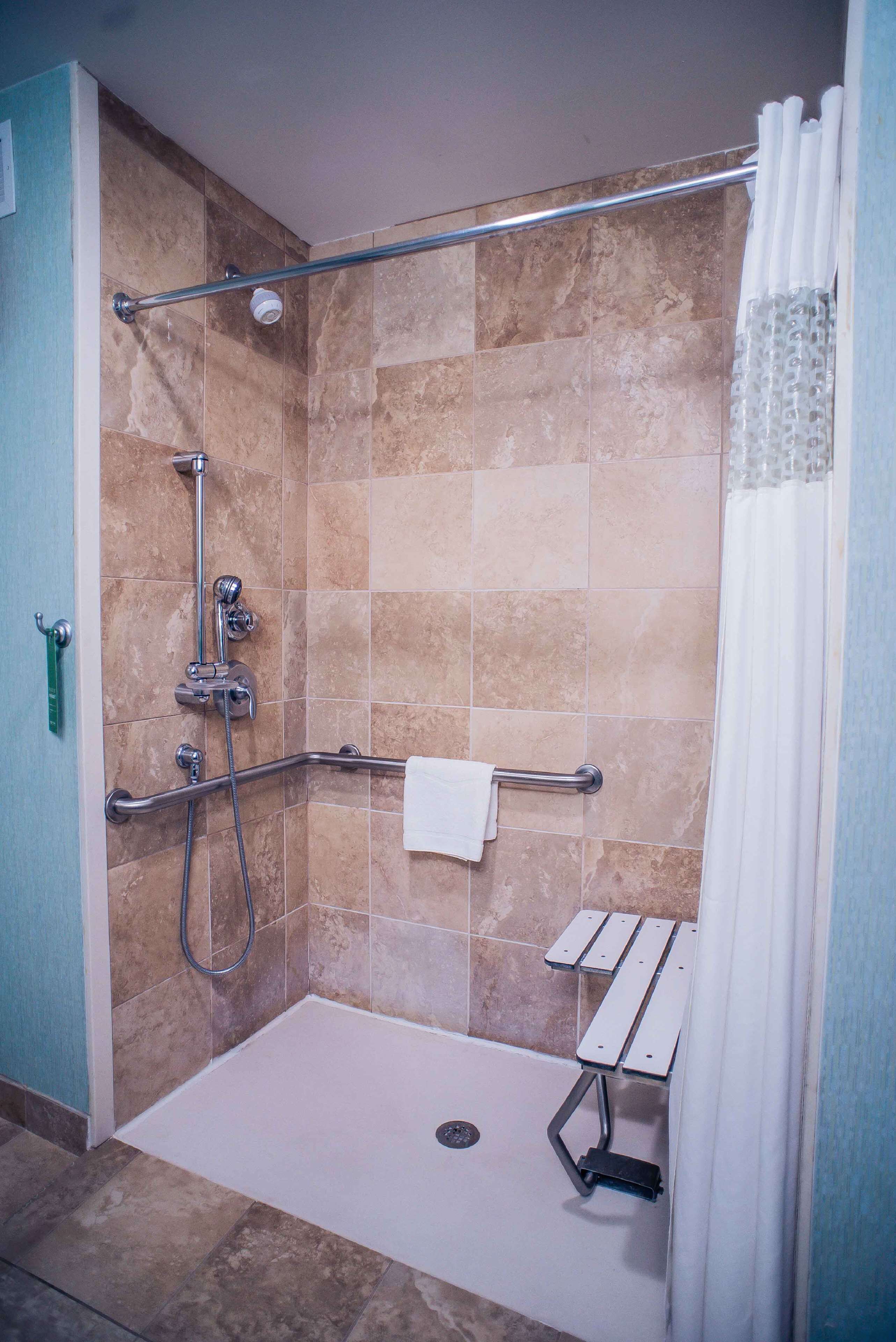Una ducha sin bordes con barra de apoyo, cabezal de ducha de mano y cortina de baño.