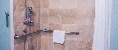 Una ducha sin bordes con barra de apoyo, cabezal de ducha de mano y cortina de baño.