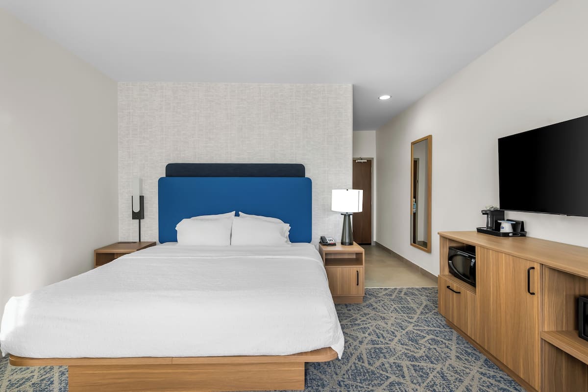 A modern hotel room with a large bed, wooden nightstands, a flat-screen TV, and a microwave.