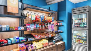 Exposição de petiscos com batatas fritas e outras opções, área refrigerada para bebidas e uma placa sobre os petiscos.
