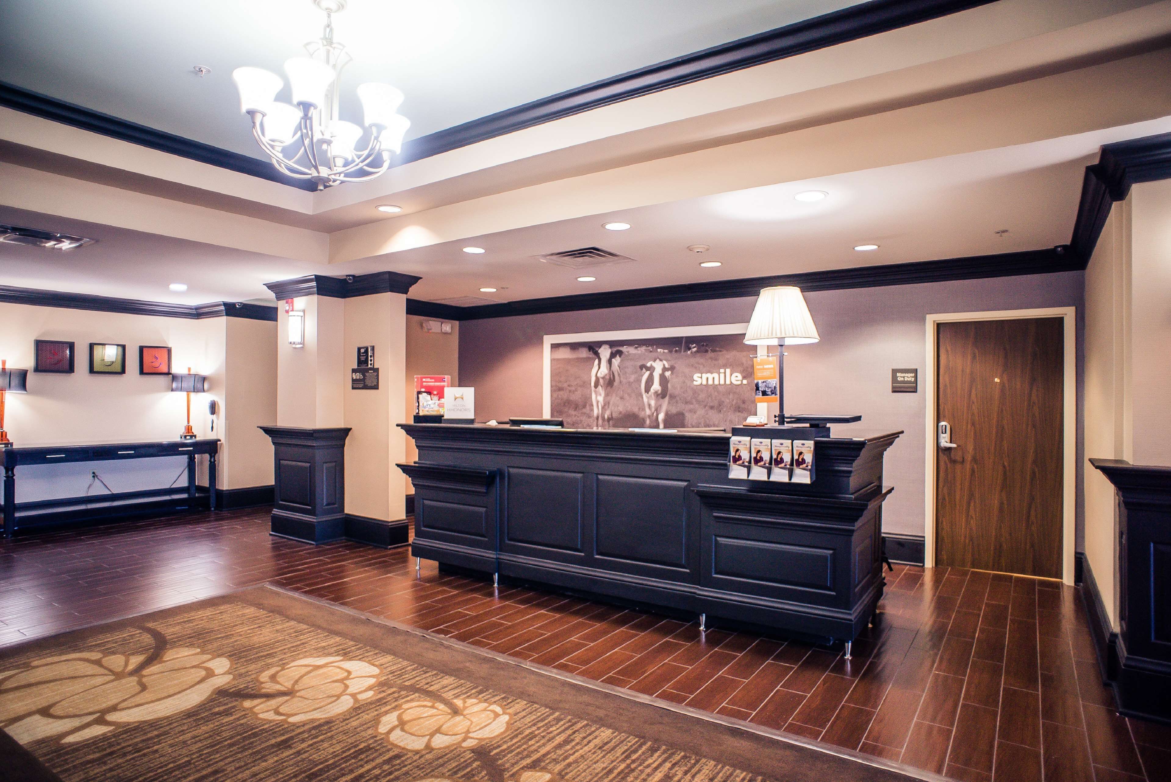 A hotel reception area with a dark reception desk, a chandelier, and a floral carpet.