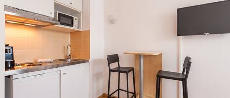 A compact kitchen with a microwave, sink, and a small dining table with two chairs.