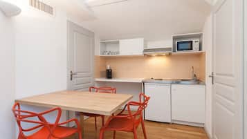 A compact kitchen with white cabinets, a microwave, a sink, and a wooden table with red chairs.