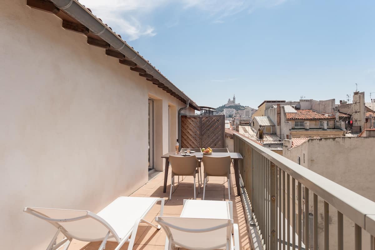 Un balcon avec une table et des chaises, une vue sur le paysage urbain et un immeuble doté d’une tour remarquable.