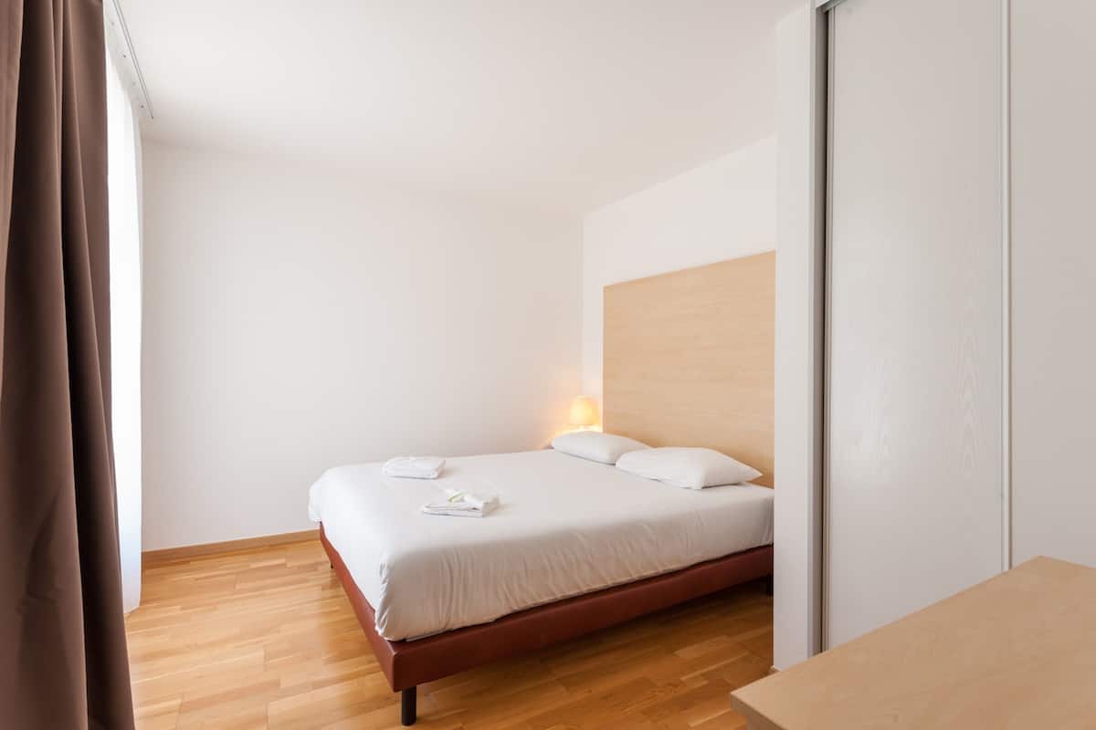 Un lit simple avec du linge de lit blanc, une tête de lit en bois et une lampe de chevet.