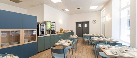 A modern dining area with blue chairs and tables, a kitchen area with appliances, and a clock on the wall.