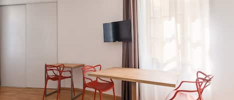 A modern room with a wooden table, two red chairs, a flat-screen TV mounted on the wall, and a sliding door.