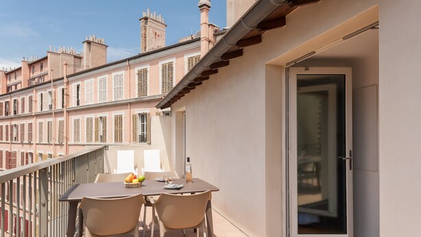 Een balkon buiten met een tafel, stoelen, een fles en een schaal fruit.