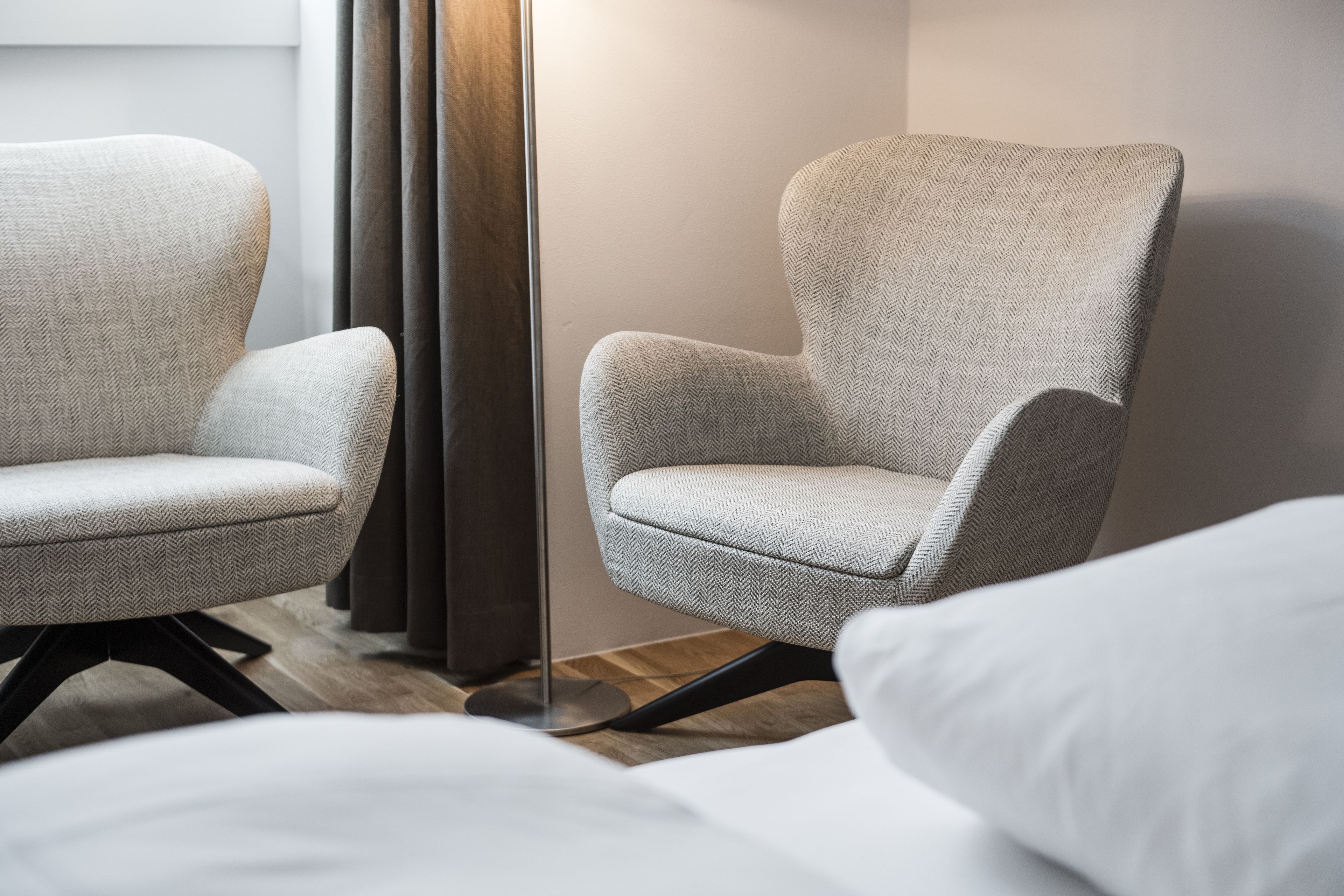 Ein modernes Hotelzimmer mit zwei gepolsterten Sessel, einer Stehlampe und einem Bett mit weißer Bettwäsche.