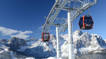 A cable car system with two gondolas suspended from a central tower, set against a backdrop of snow-covered mountains and clear blue sky.