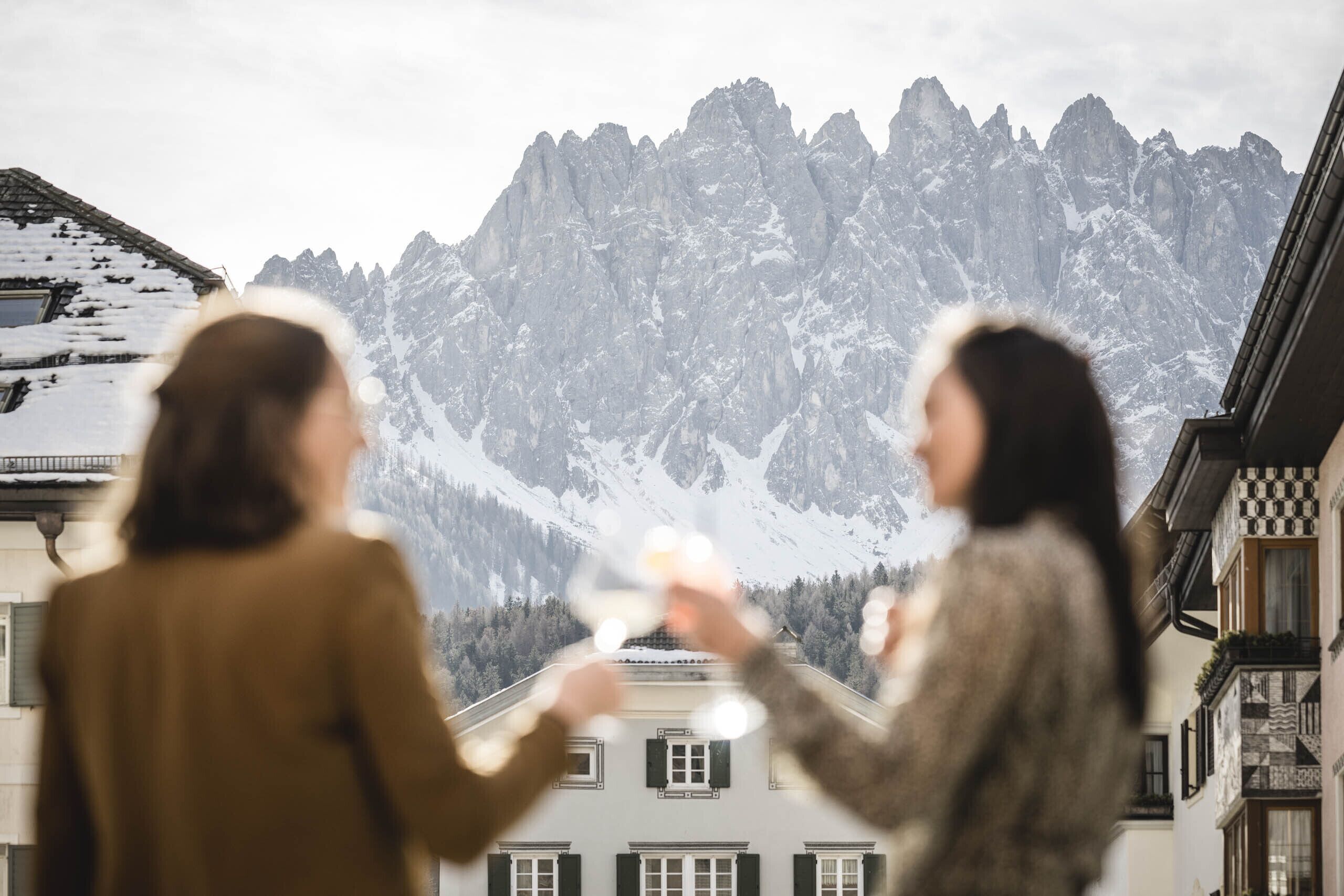 Two people toasting with wine glasses in front of a mountain backdrop.