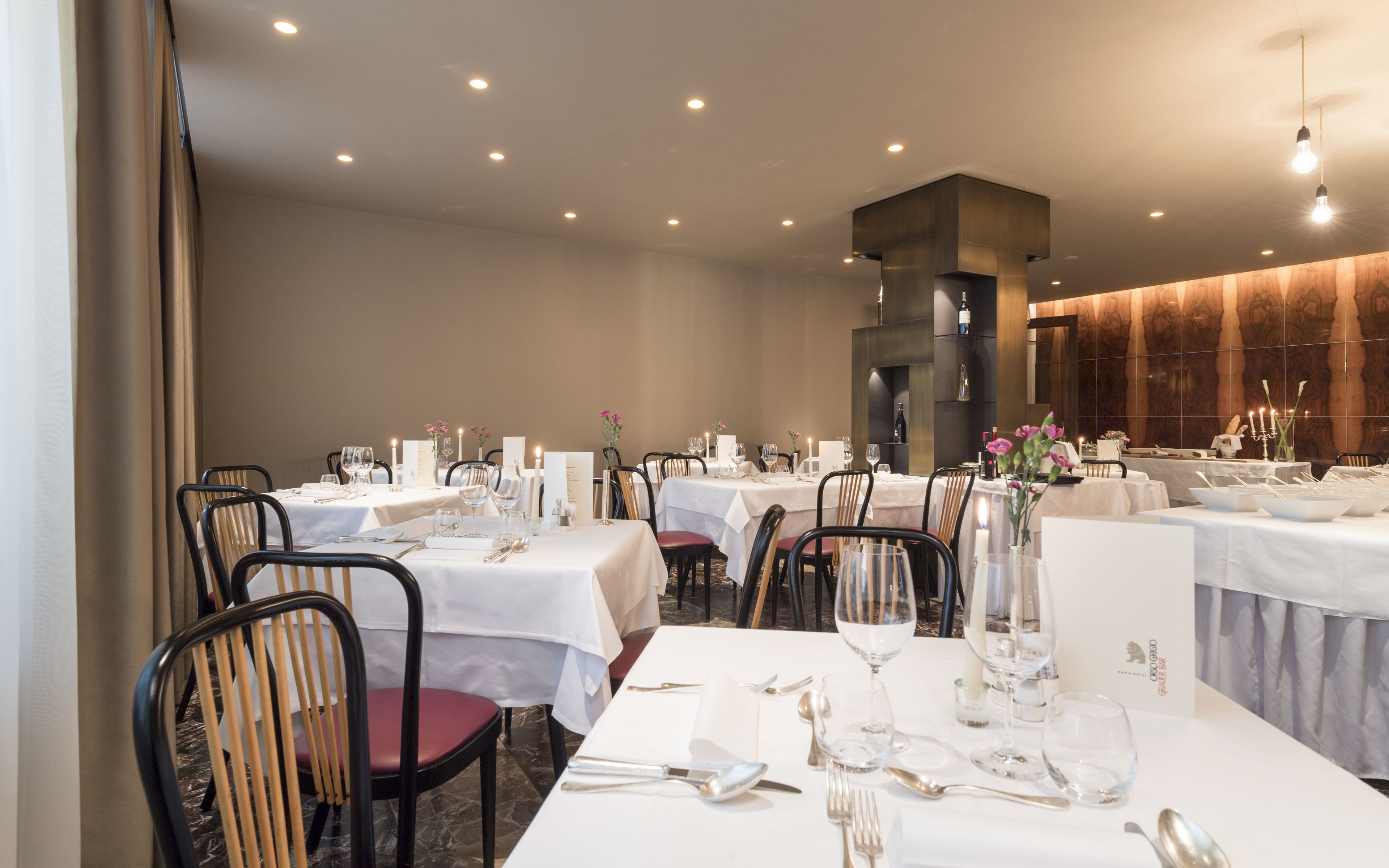 Un restaurante con varias mesas dispuestas para comer, con manteles blancos y velas.