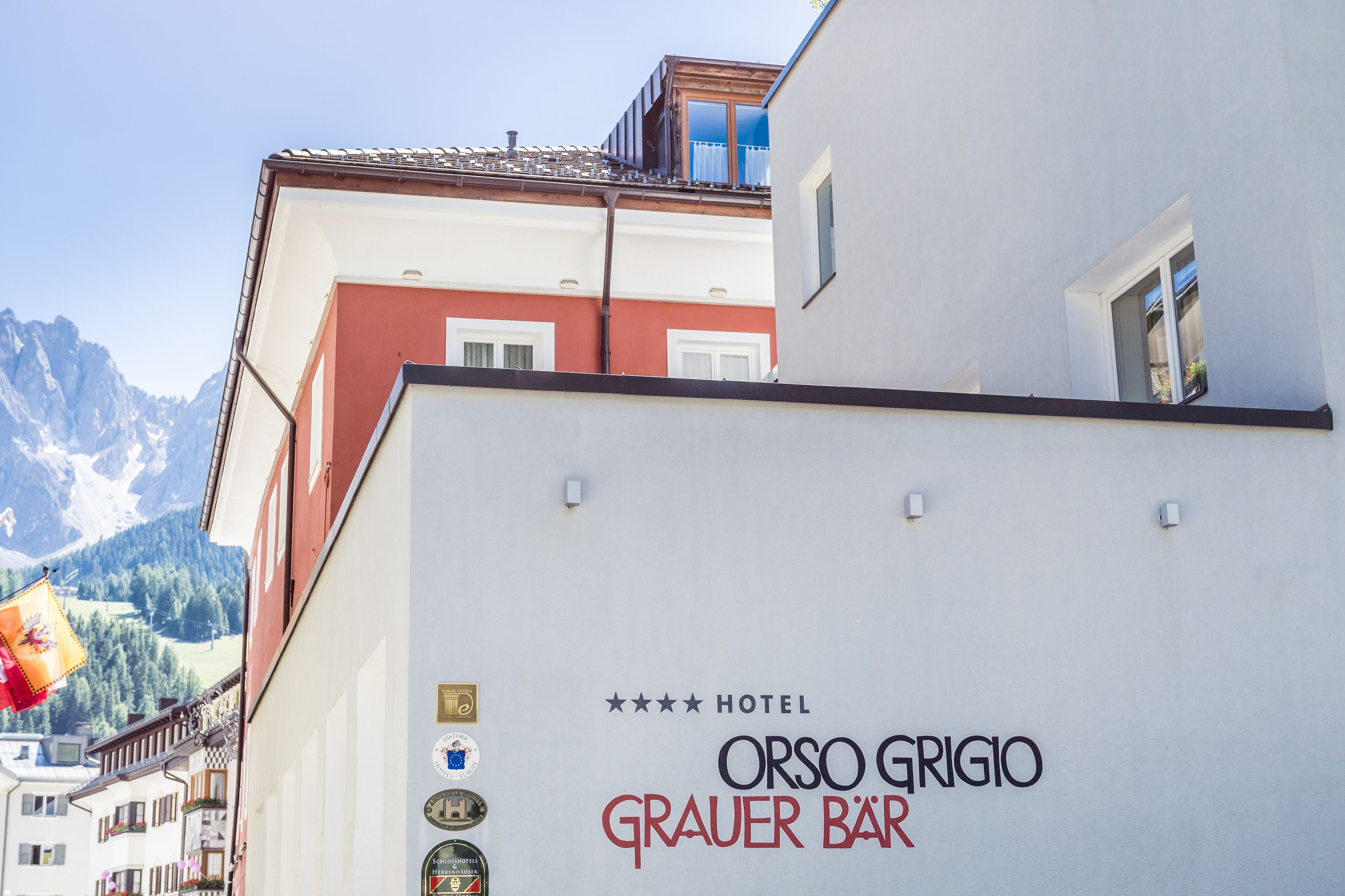 Hotelansicht mit der Aufschrift 'Orso Grigio Grauer Bar' und mehreren Auszeichnungen.