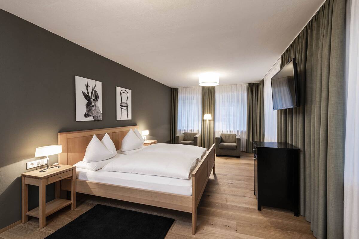 A hotel room with a bed, bedside tables, a desk, a chair, a TV, and curtains.