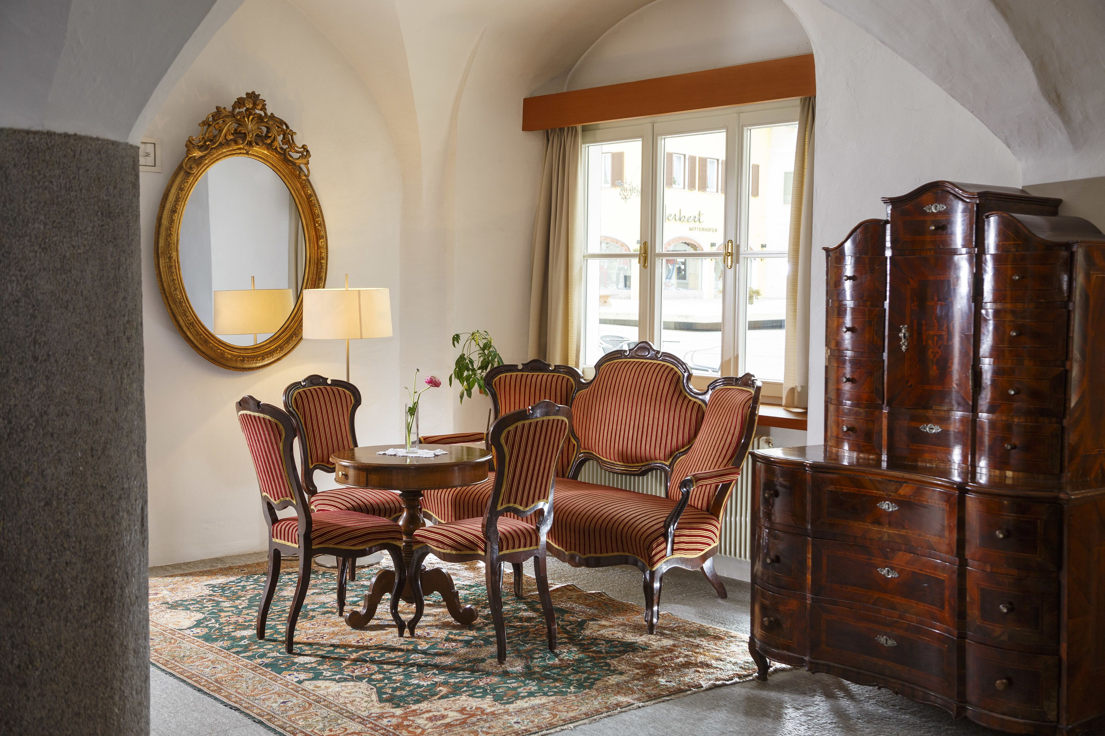 Un coin repas avec une table ronde, des chaises à rayures, un miroir et un buffet en bois.