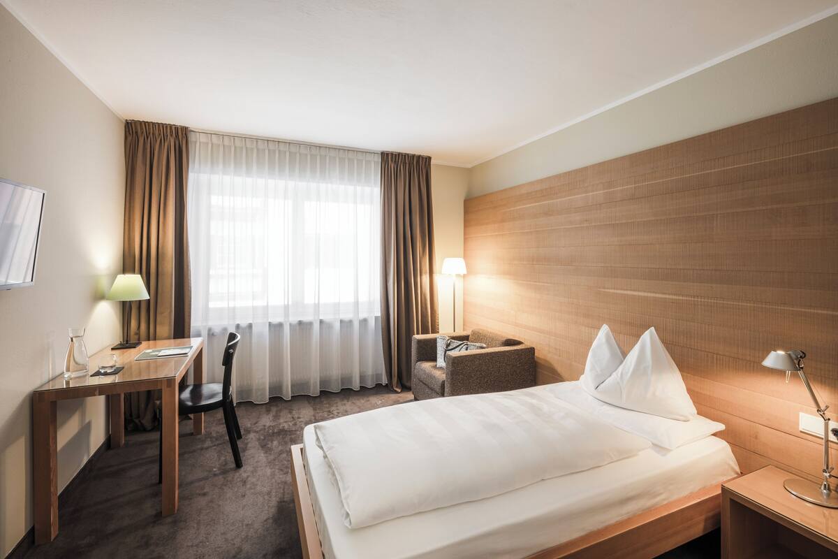 A hotel room with a bed, desk, chair, TV, and two bedside lamps.