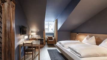 A hotel room with a wooden desk, two beds, a TV, and a window with curtains.
