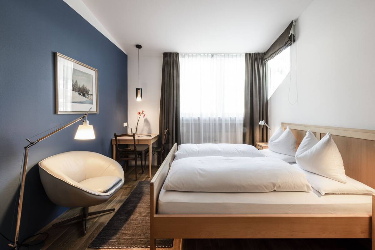 A hotel room with a bed, bedside tables, a desk, a chair, a lamp, and a framed picture on the wall.