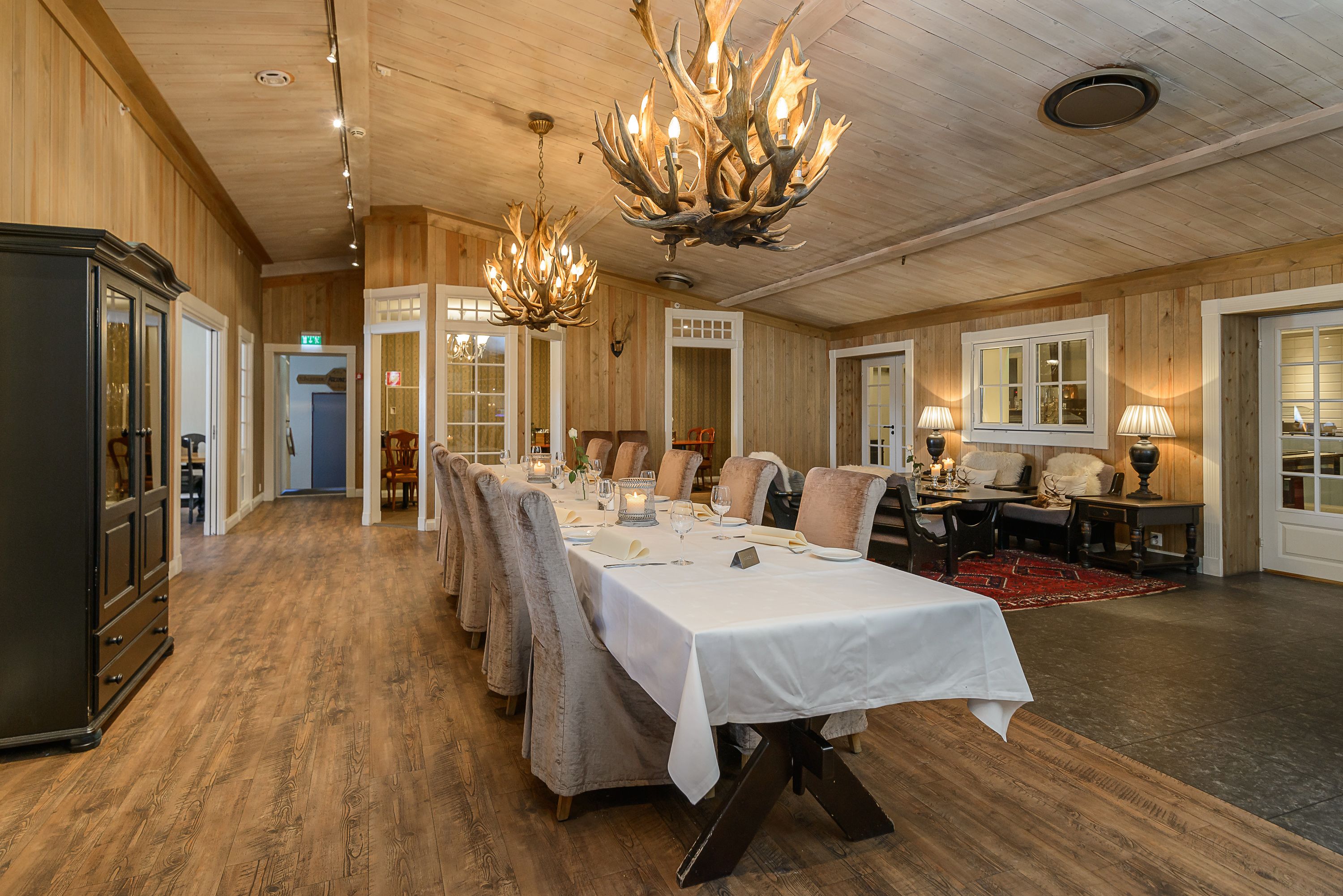 Un comedor con una larga mesa dispuesta para una comida, paredes de madera y candelabros.