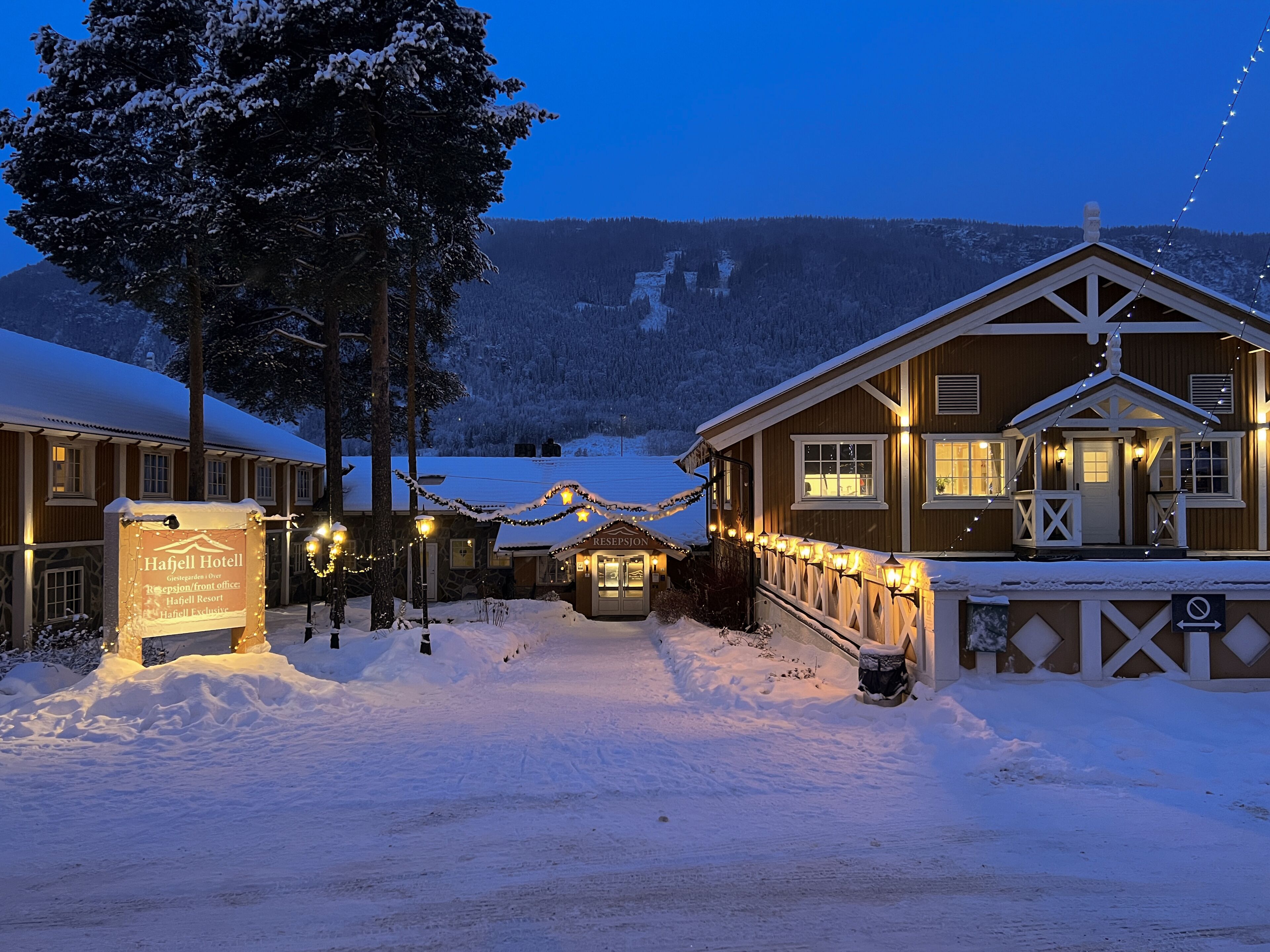 Un hotel cubierto de nieve con recepción, habitaciones de huéspedes y montañas al fondo.