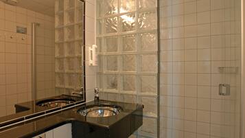 Un baño con lavamanos doble, un espejo grande y una pared de bloques de vidrio.