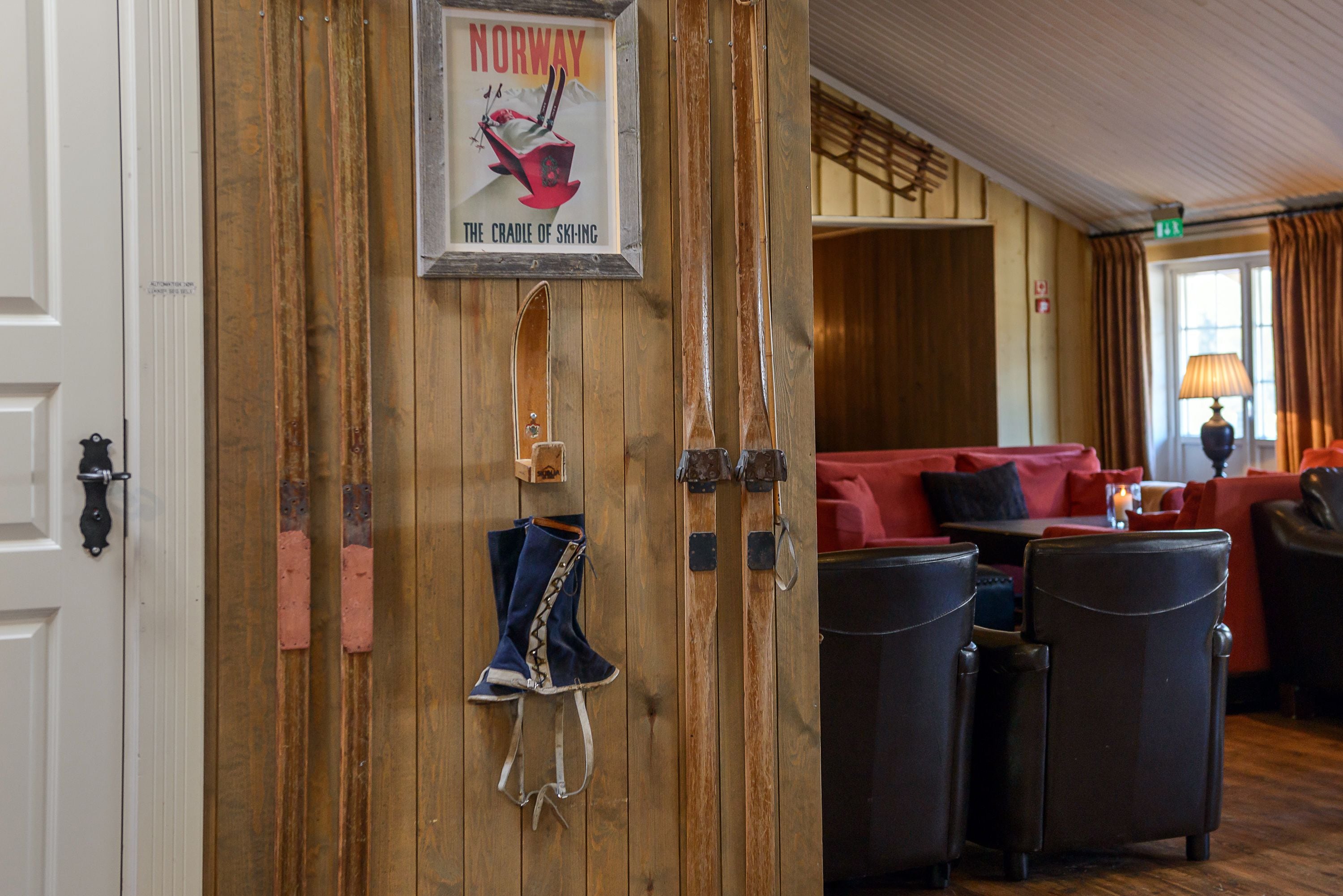 A wooden wall with a framed sign, a door, and a seating area with red cushions and black chairs.