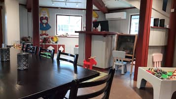 A dining area with a wooden table and chairs, a window with natural light, and a wall with children's toys and a mural.