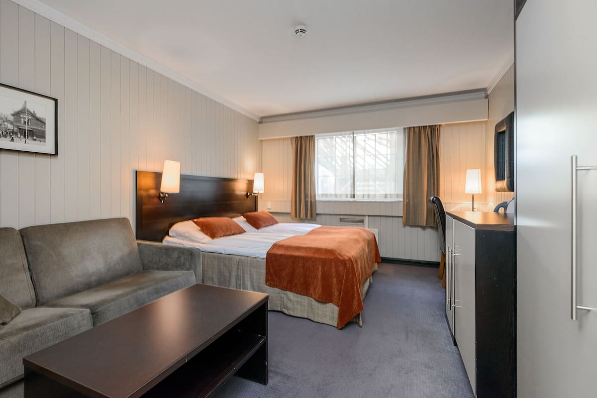 A hotel room with a bed, a sofa, a desk, a TV, and a window with curtains.