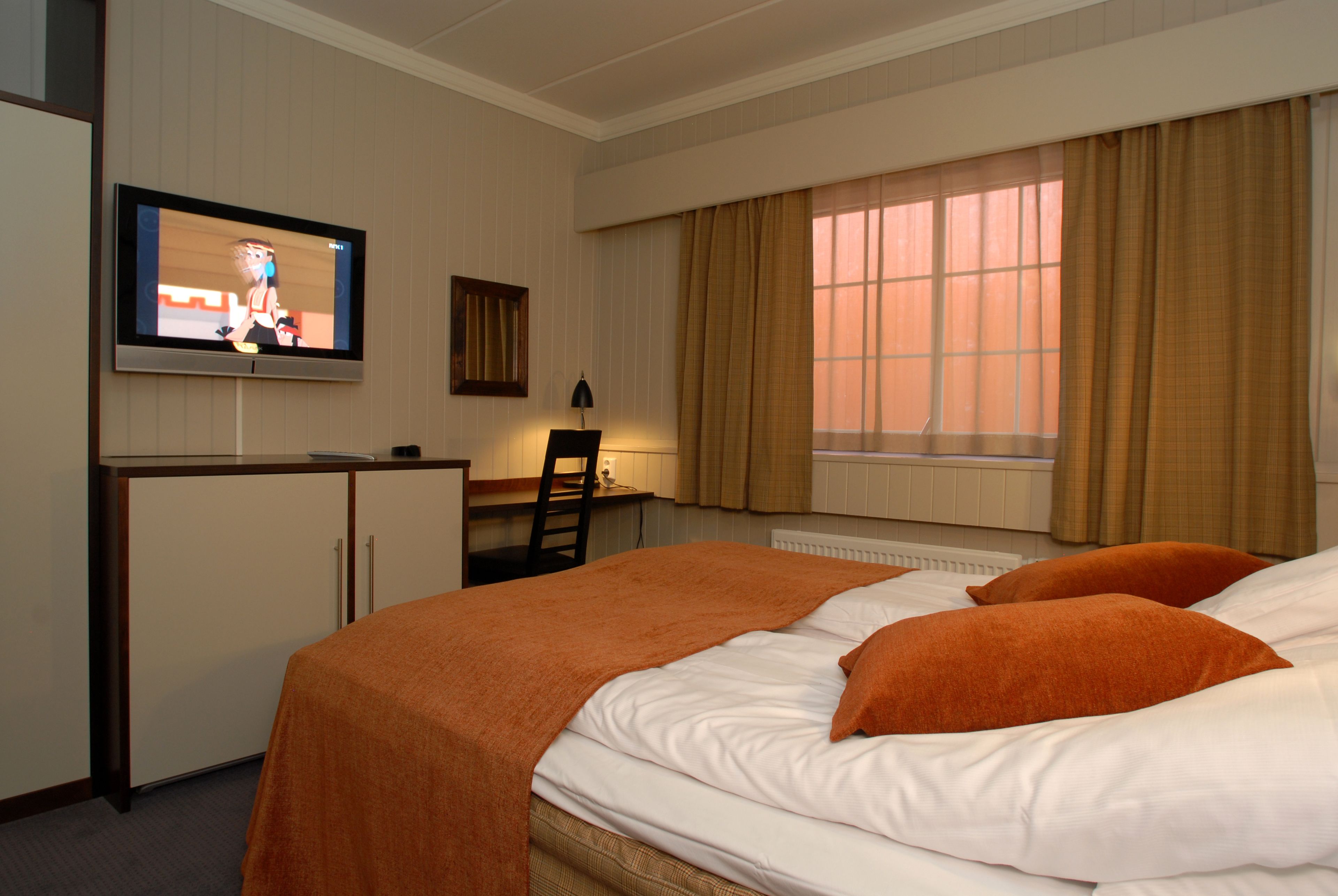 A hotel room with a bed, a desk, a television, and a window with curtains.