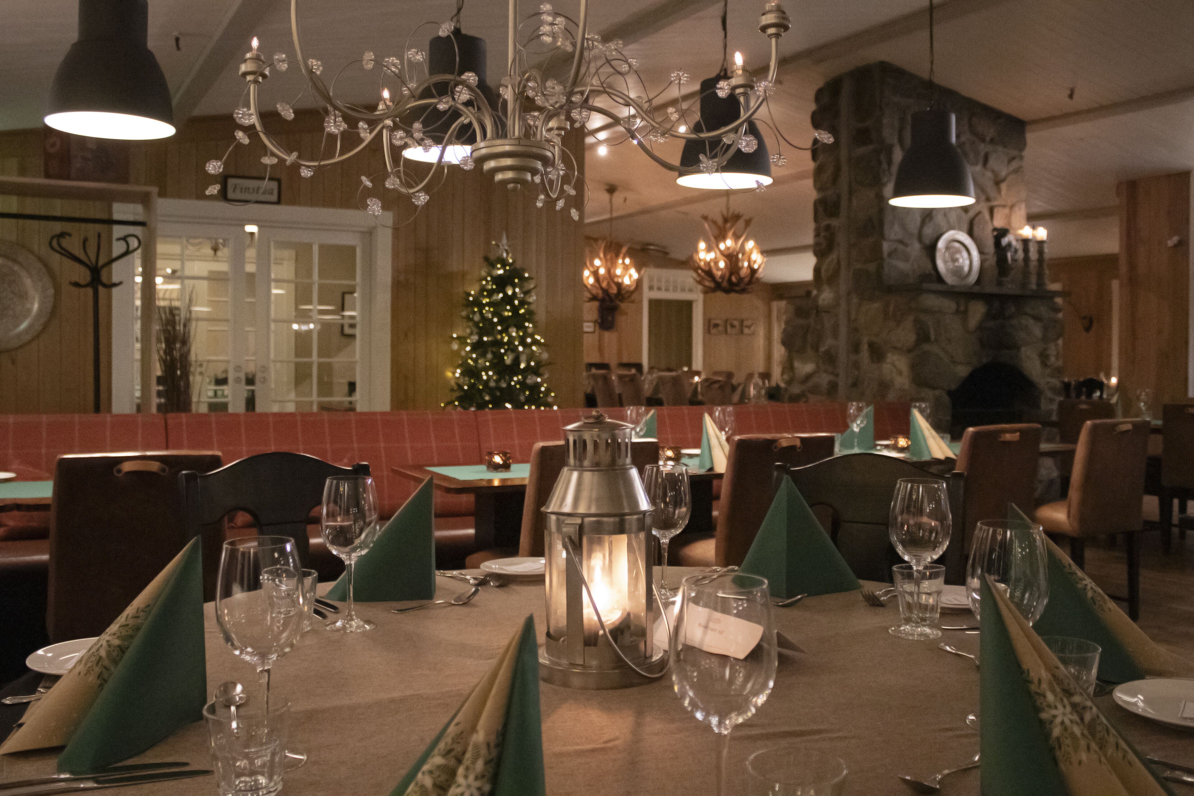 Ein Restaurant mit Weihnachtsbaum, stimmungsvoll beleuchteten Tischen und einem Steinkamin.