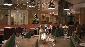 Ein Restaurant mit Weihnachtsbaum, stimmungsvoll beleuchteten Tischen und einem Steinkamin.