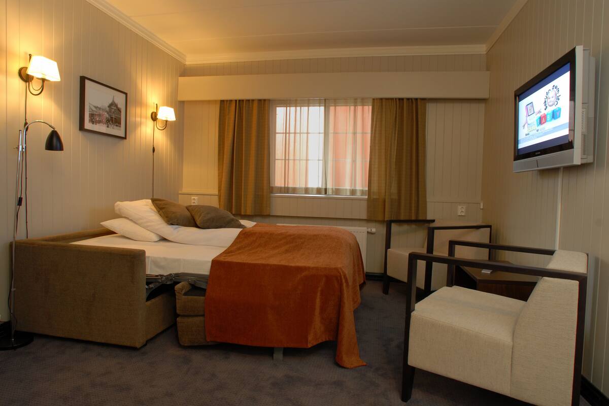 A hotel room with a bed, a sofa, a chair, a desk, and a TV.