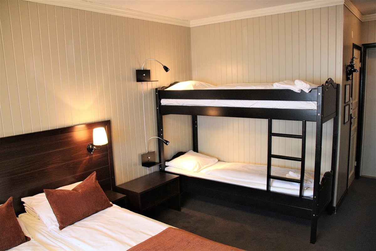 A bunk bed with a nightstand and a wall-mounted lamp.