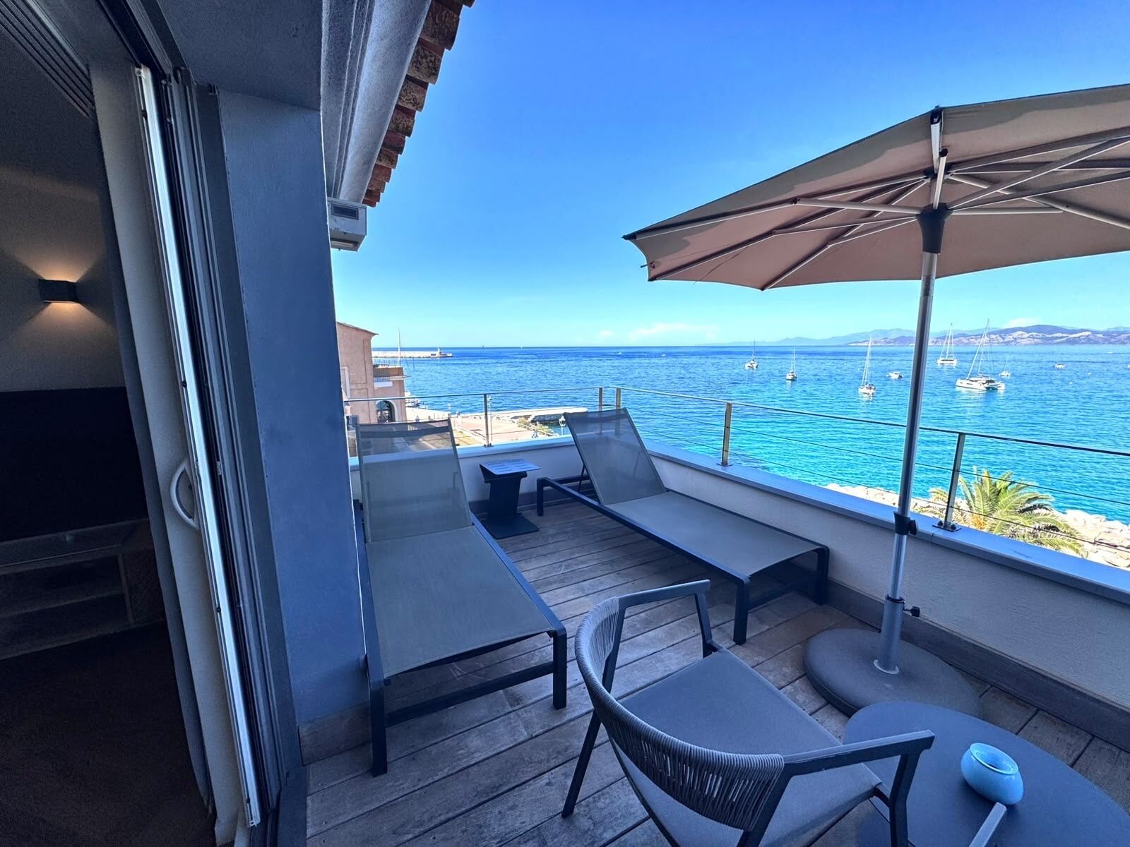 Un balcón con mobiliario exterior, vista al mar y cielo despejado.