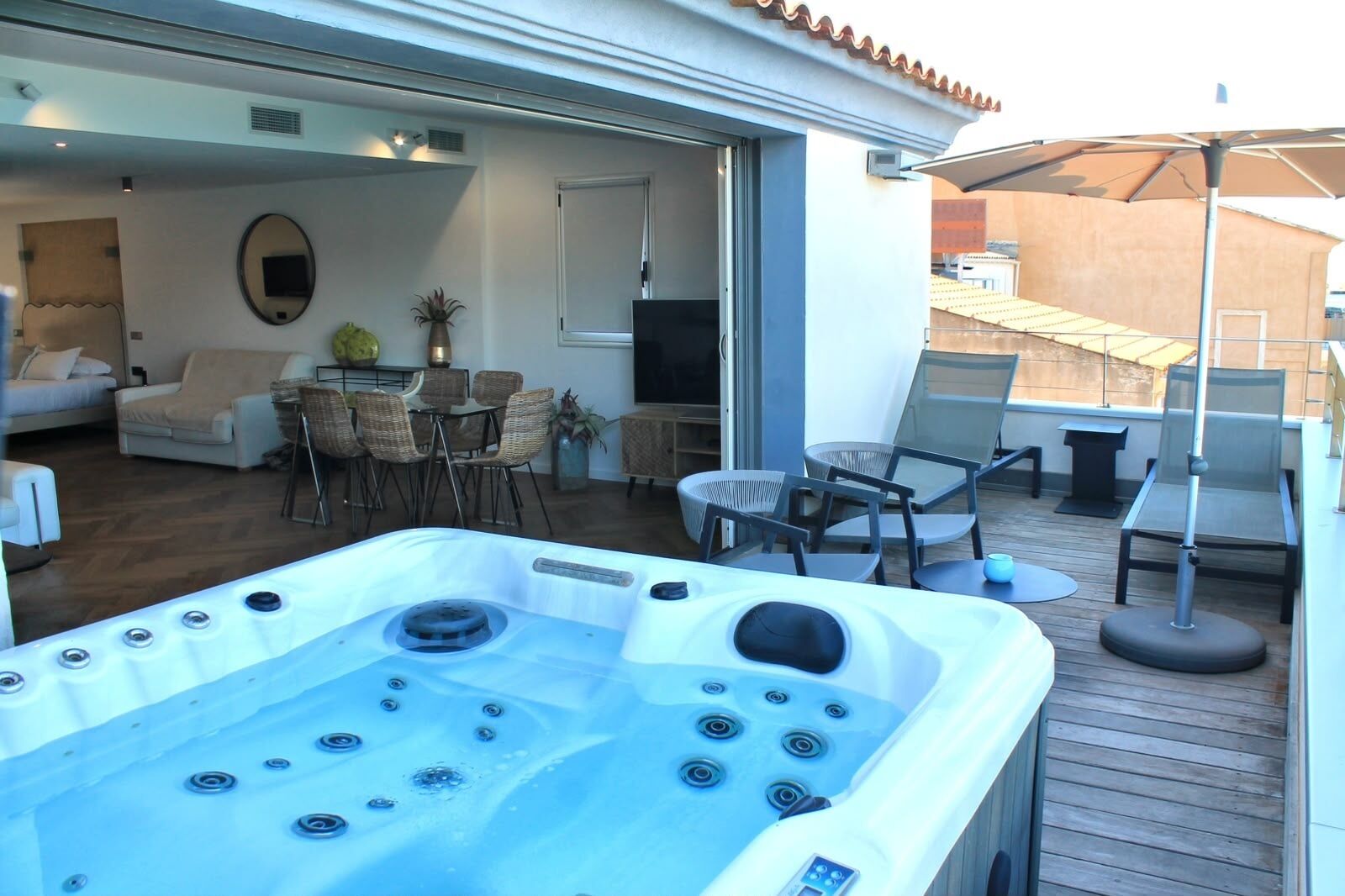 A hot tub with multiple jets, a dining area with wicker chairs, and a TV mounted on the wall.