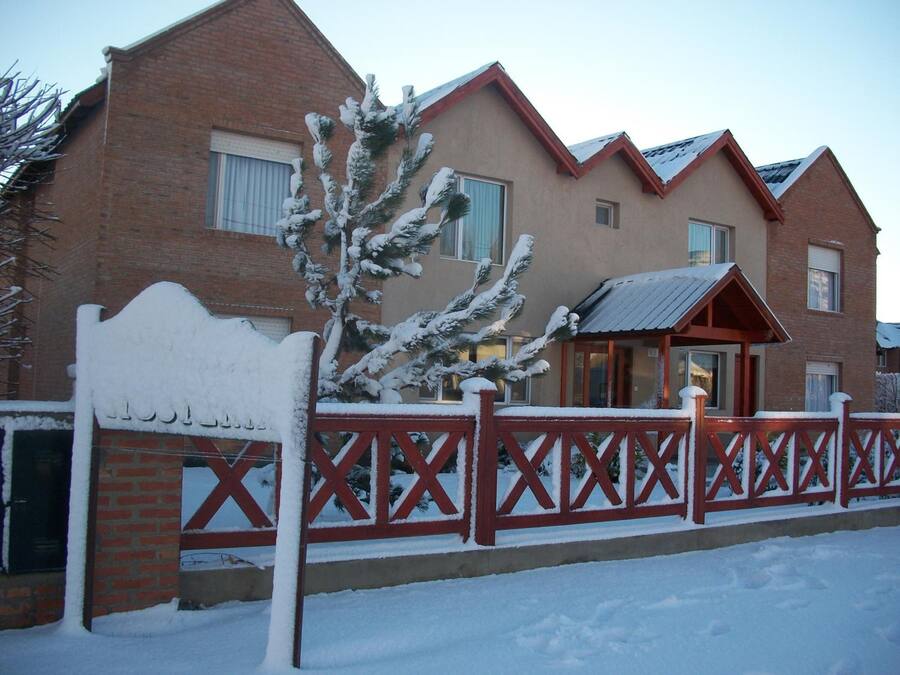 A brick building with a red fence and snow-covered trees.