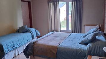 A bedroom with two beds, a window with curtains, and a wooden ceiling.